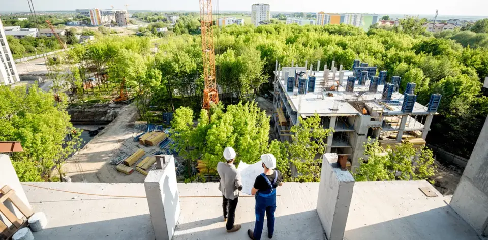 two construction workers on the top if a building looking at drawings