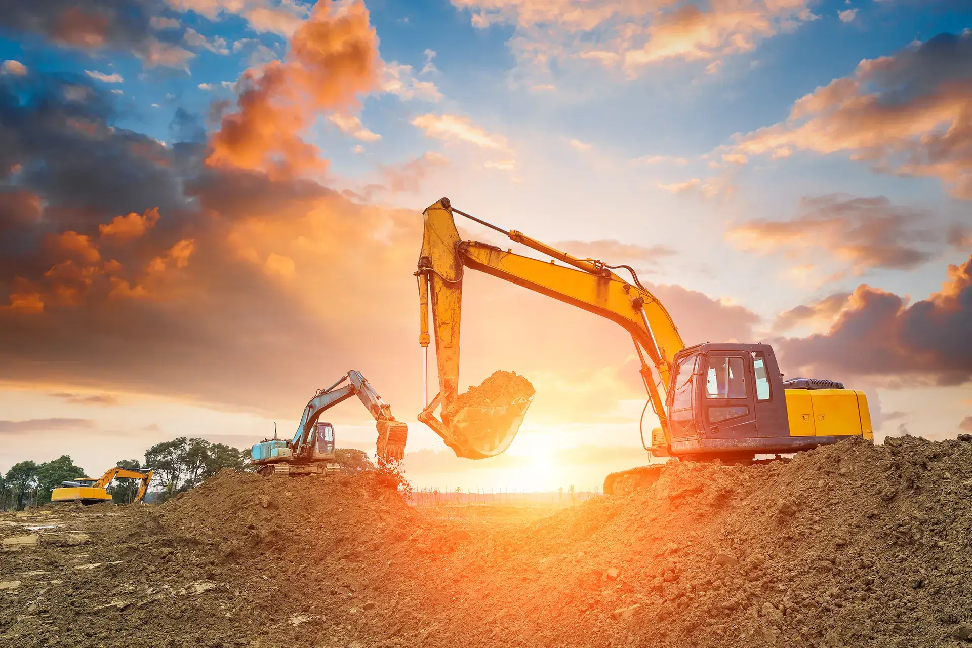 excavator moving dirt with a sunset in the background