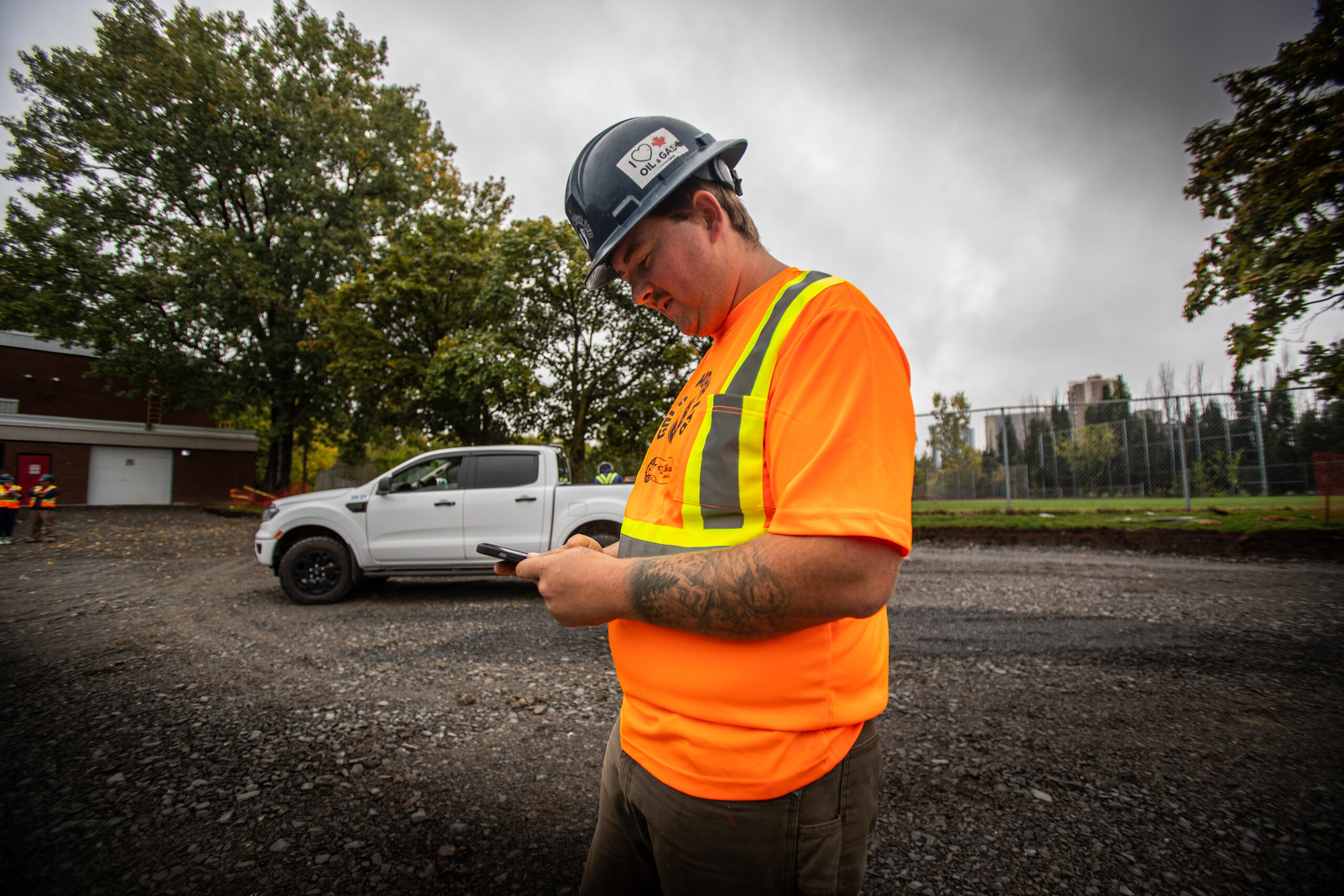 Worker in hi-visibility vest and hard hat enters jobsite info on phone.